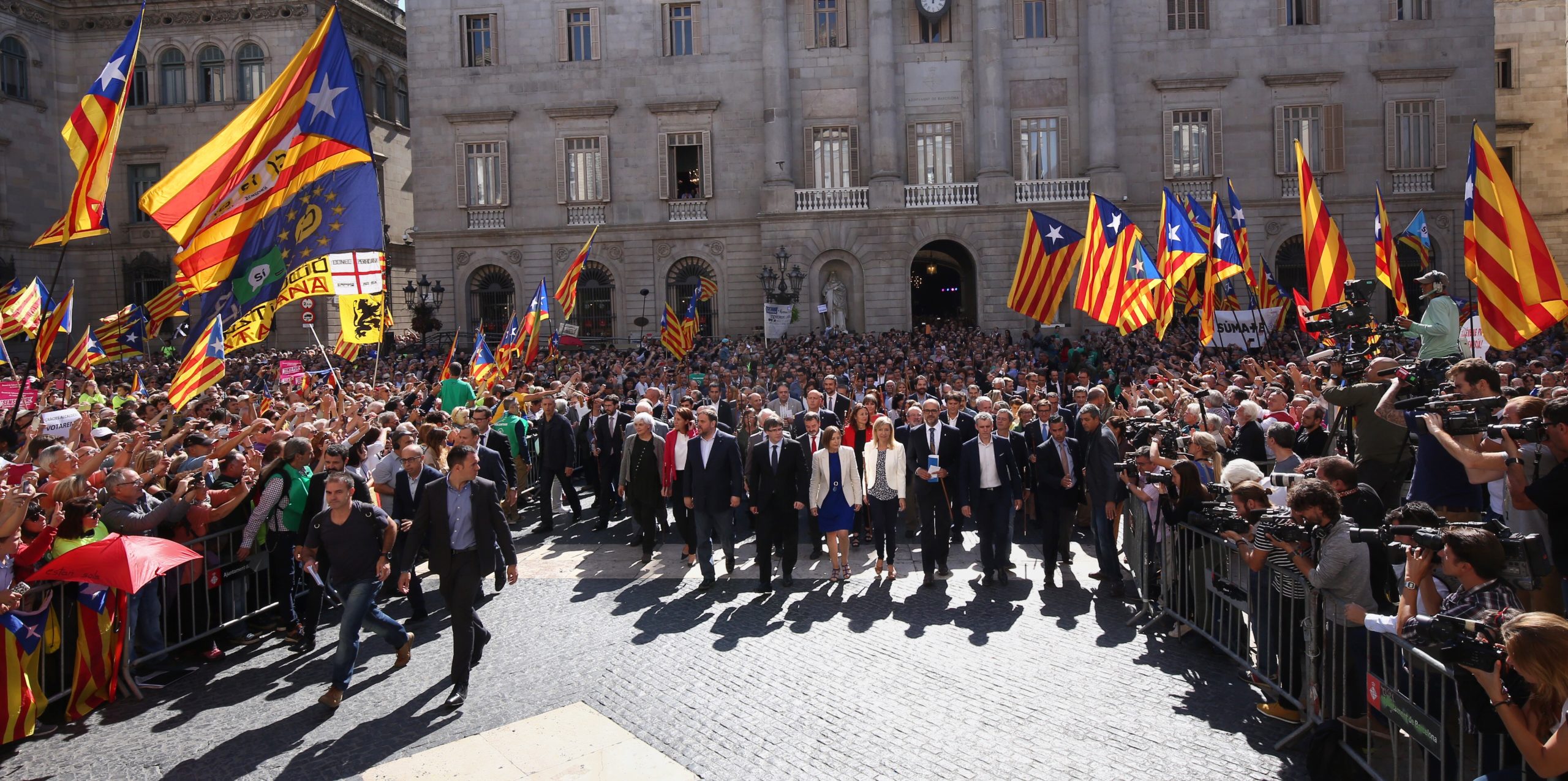 En rekke dresskledde mennesker går sammen gjennom et folkehav der flere veiver det katalanske flagget.