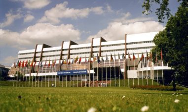 Bilde av fasaden til Europarådet med skiltet og alle medlemslandenenes flagg hengende utenfor.