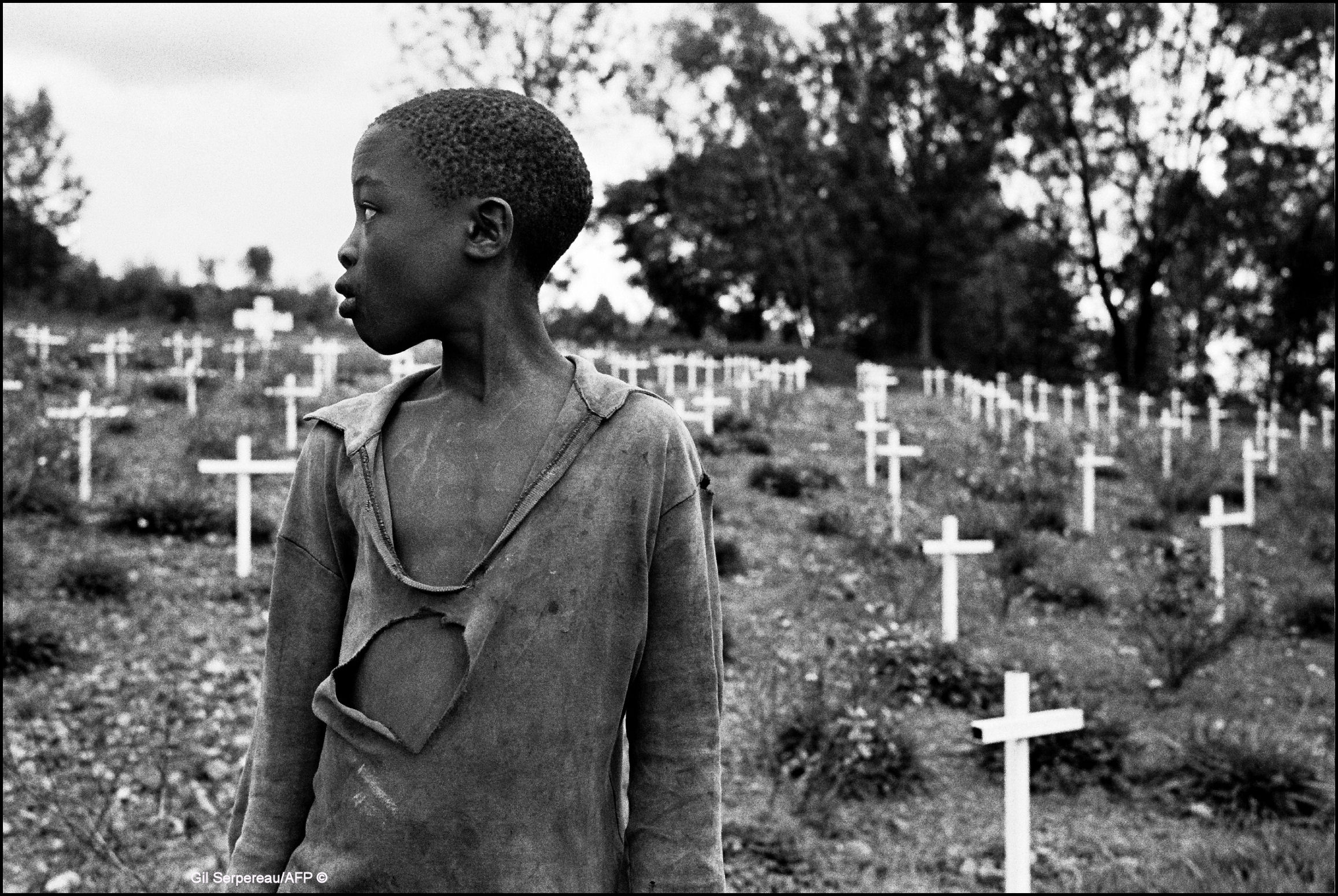 Et barn i slitte klær står foran et kirkegård fylte med enkle hvite kors