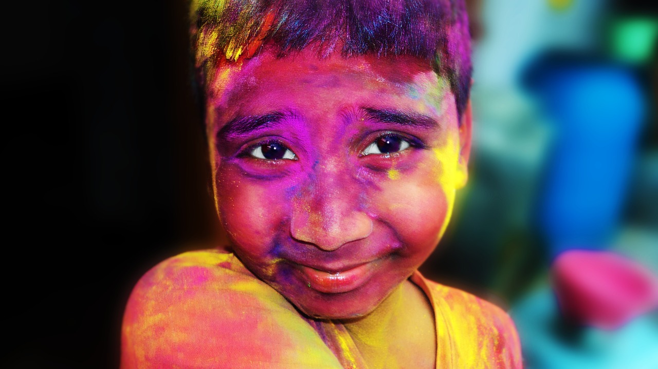 Nærbilde av en liten gutt som smiler til kamera. Han er dekket i malingspulver i forskjellige farger. Under Holifestivalen kaster man fargepulver på hverandre.