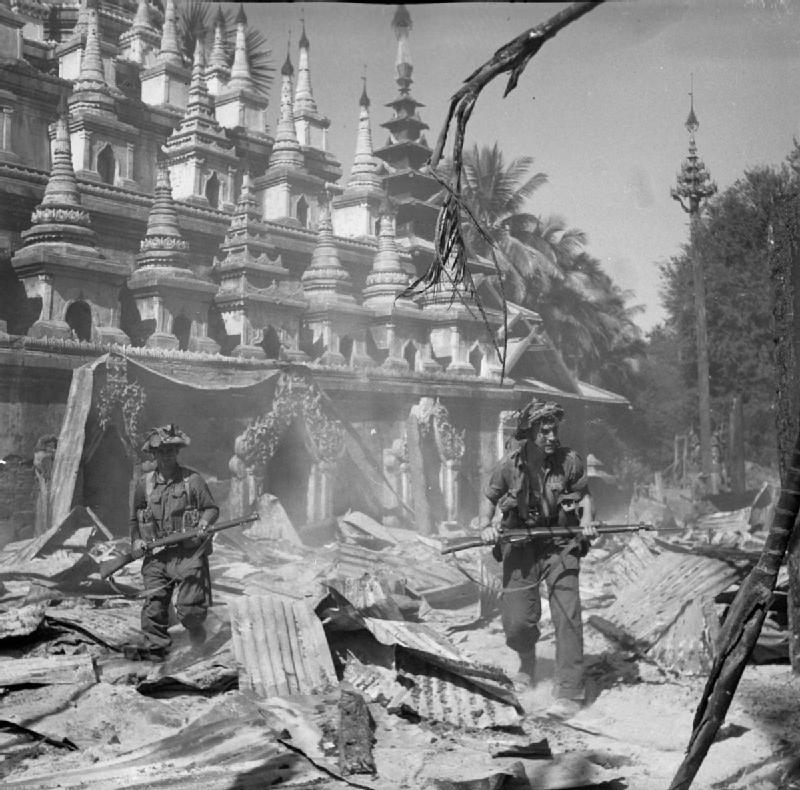 svart-hvitt bilde av noen soldater som går foran en tradisjonell bygning og ruiner