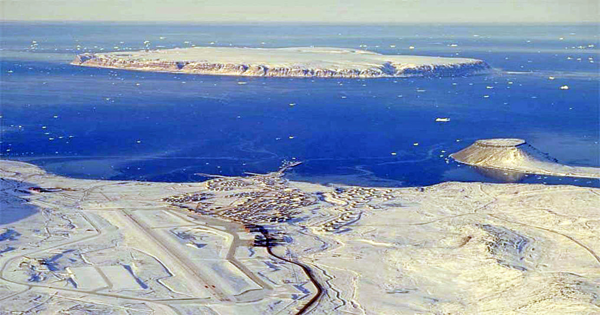 Flyfoto av snødekt landskap der man kan se et utbygd område nært sjøen.