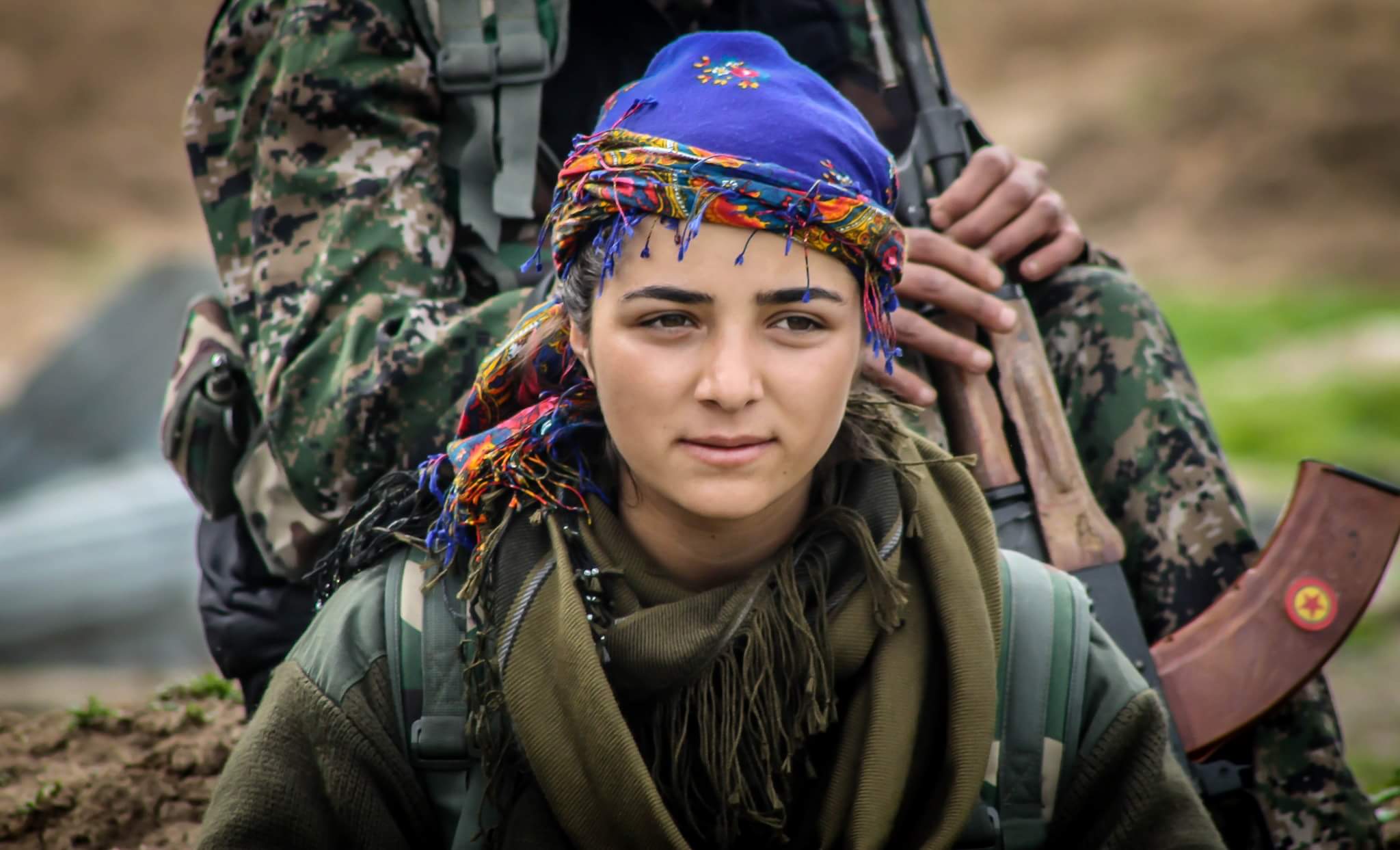 En ung kvinne, kledd i militæruniform og med et fargerikt sjal på hodet, har blikket målrettet festet til høyre for kameraet.