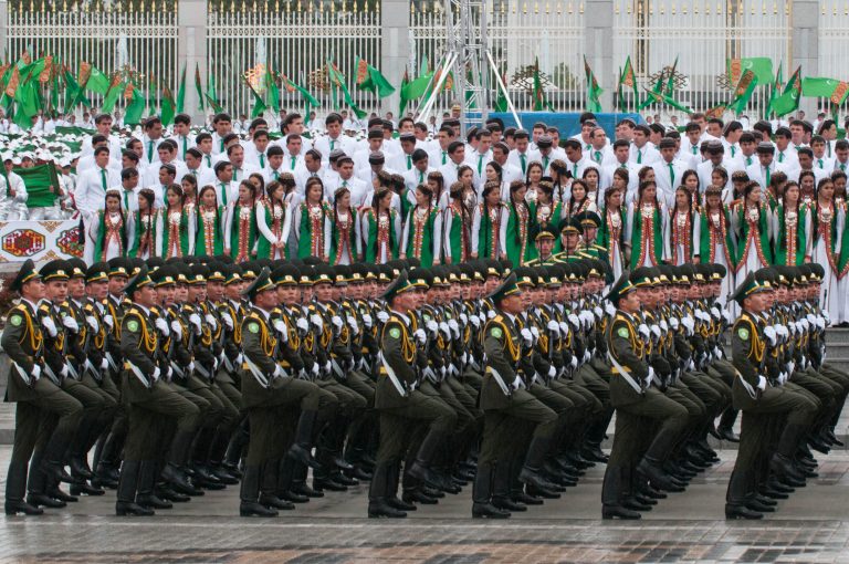 Militærparade. I bakgrunnen veiver hvitkledde mennesker med det turkmenske flagget