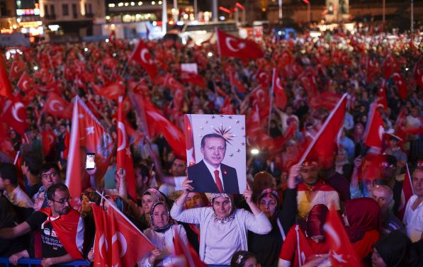 Folkemengde samlet på en plass, alle veiver tyrkiske flagg og en dame holder opp en plakat med bilde av Erdogan