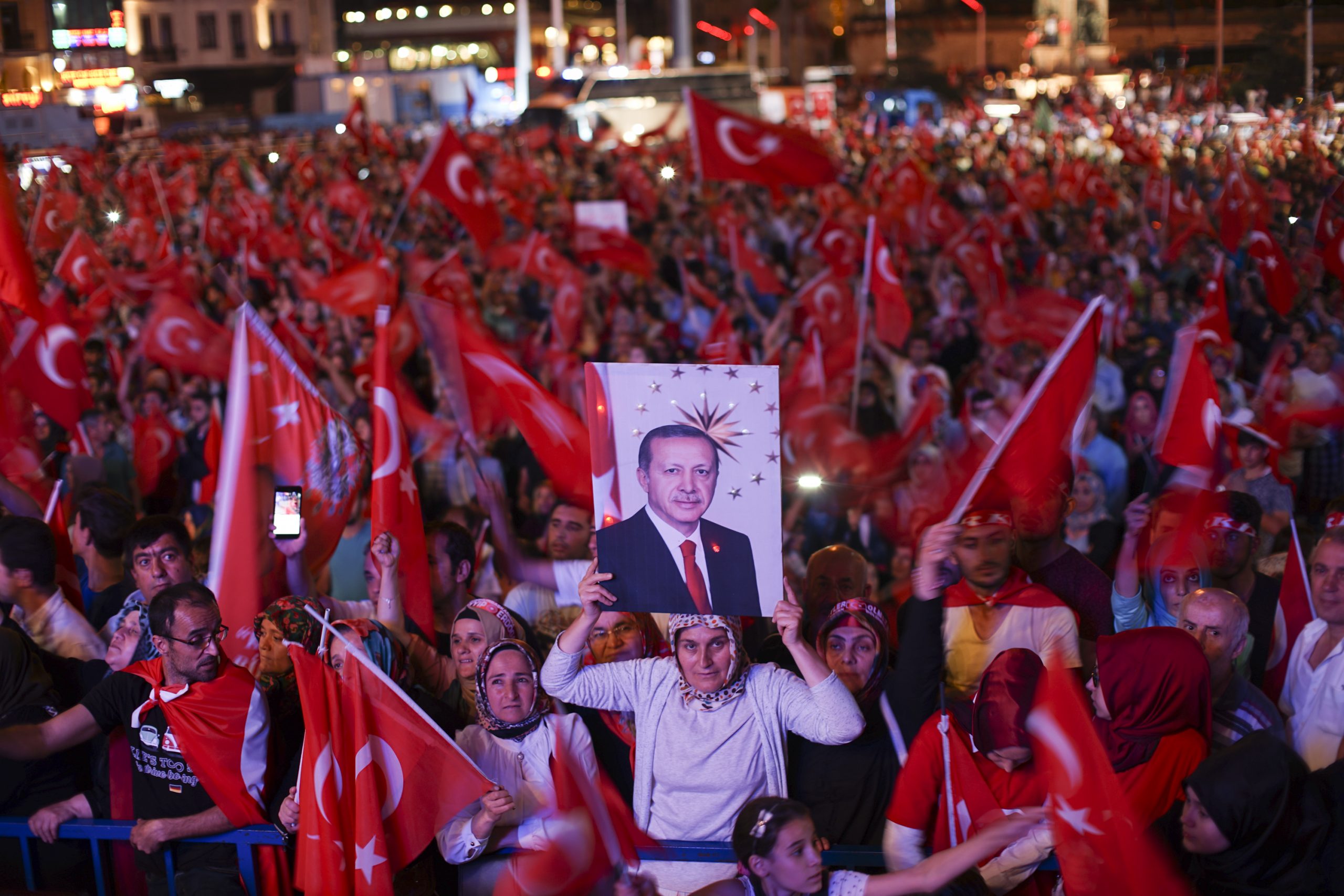 Folkemengde samlet på en plass, alle veiver tyrkiske flagg og en dame holder opp en plakat med bilde av Erdogan