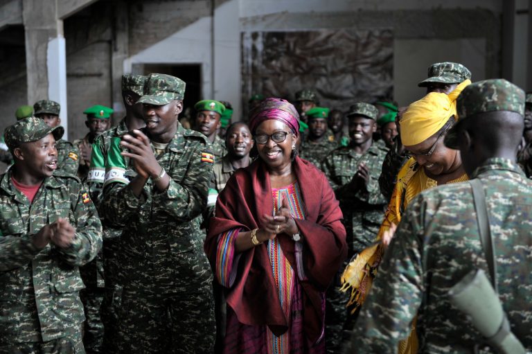 En blid kvinne står i sentrum av bilde, rundt henne er soldater som klapper