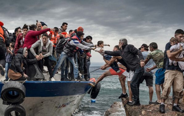 Mennesker er på vei over fra en overfylt åpen båte til land.