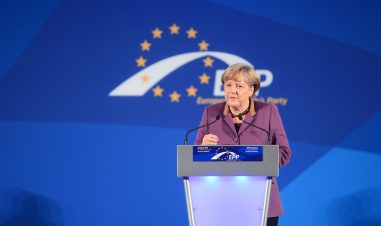 Angela Merkel taler fra en talerstoler. I bakgrunnen ser men EU-stjernene.