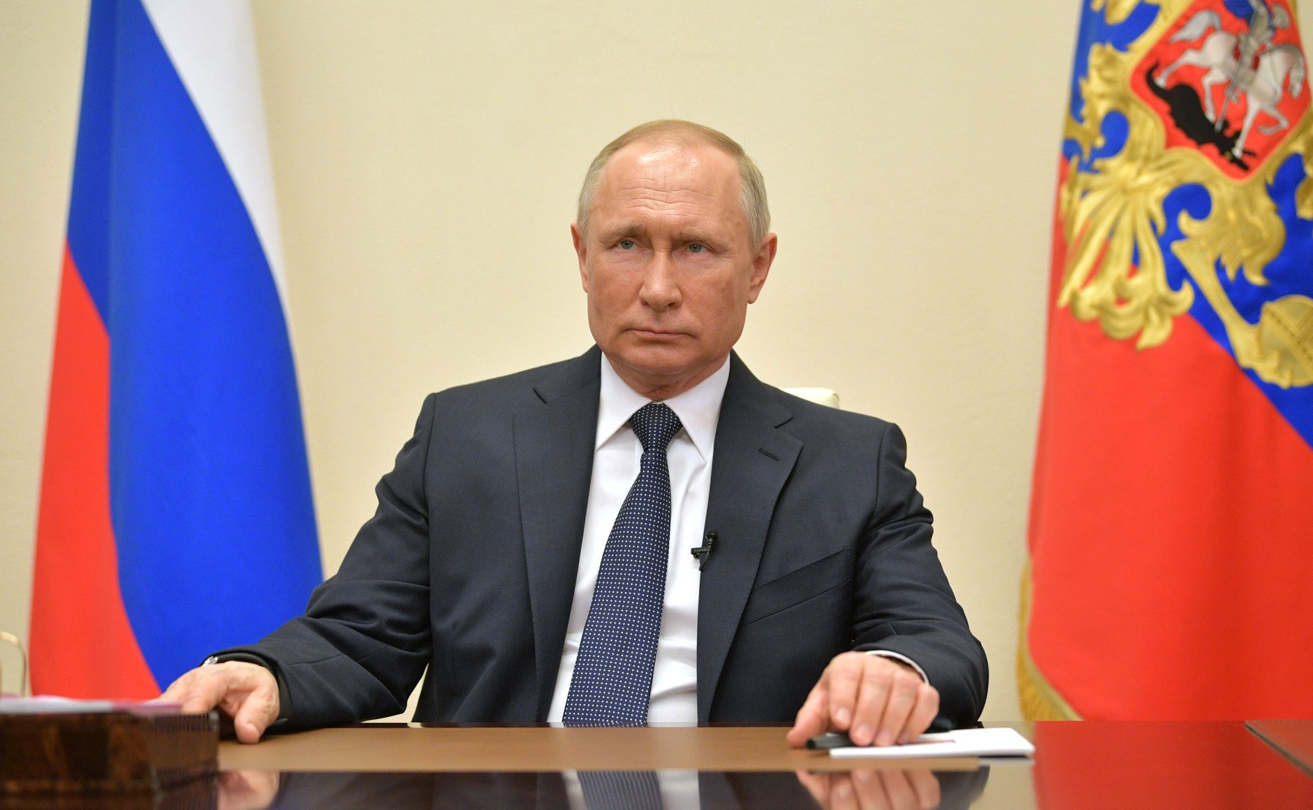 Putin sitter ved en pult med det russiske flagget bak seg