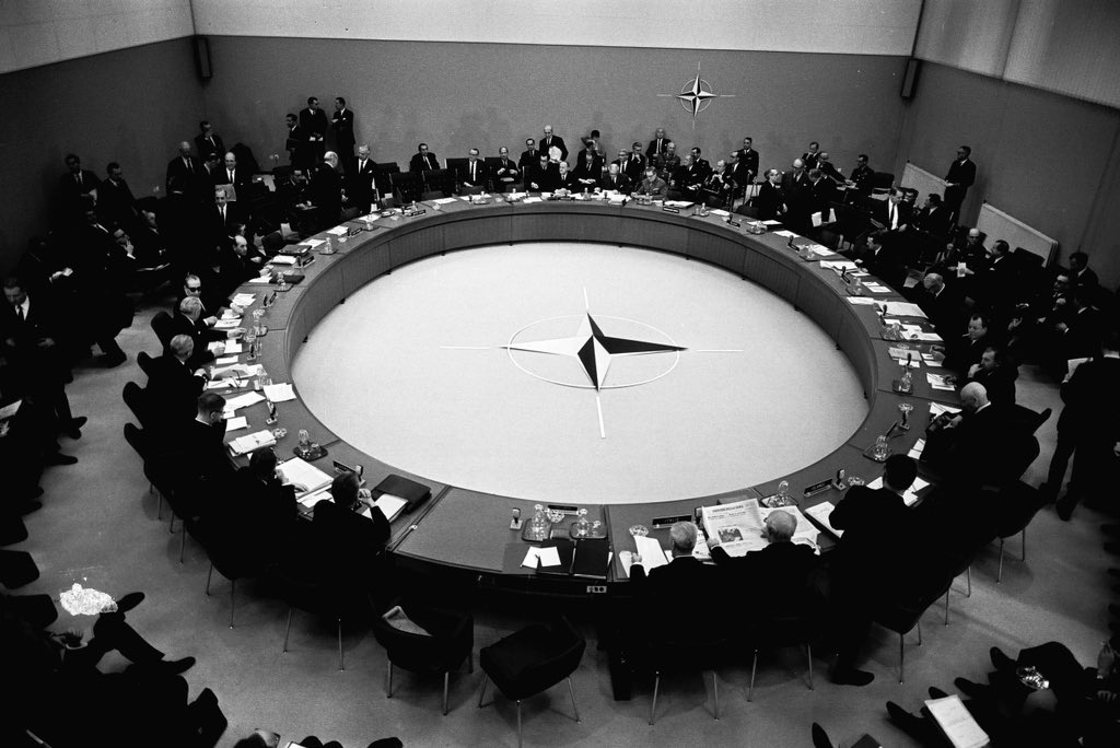 Ministrene for NATOs medlemsland sitter rundt det runde bordet, med NATOs stjerneformede logo i midten.