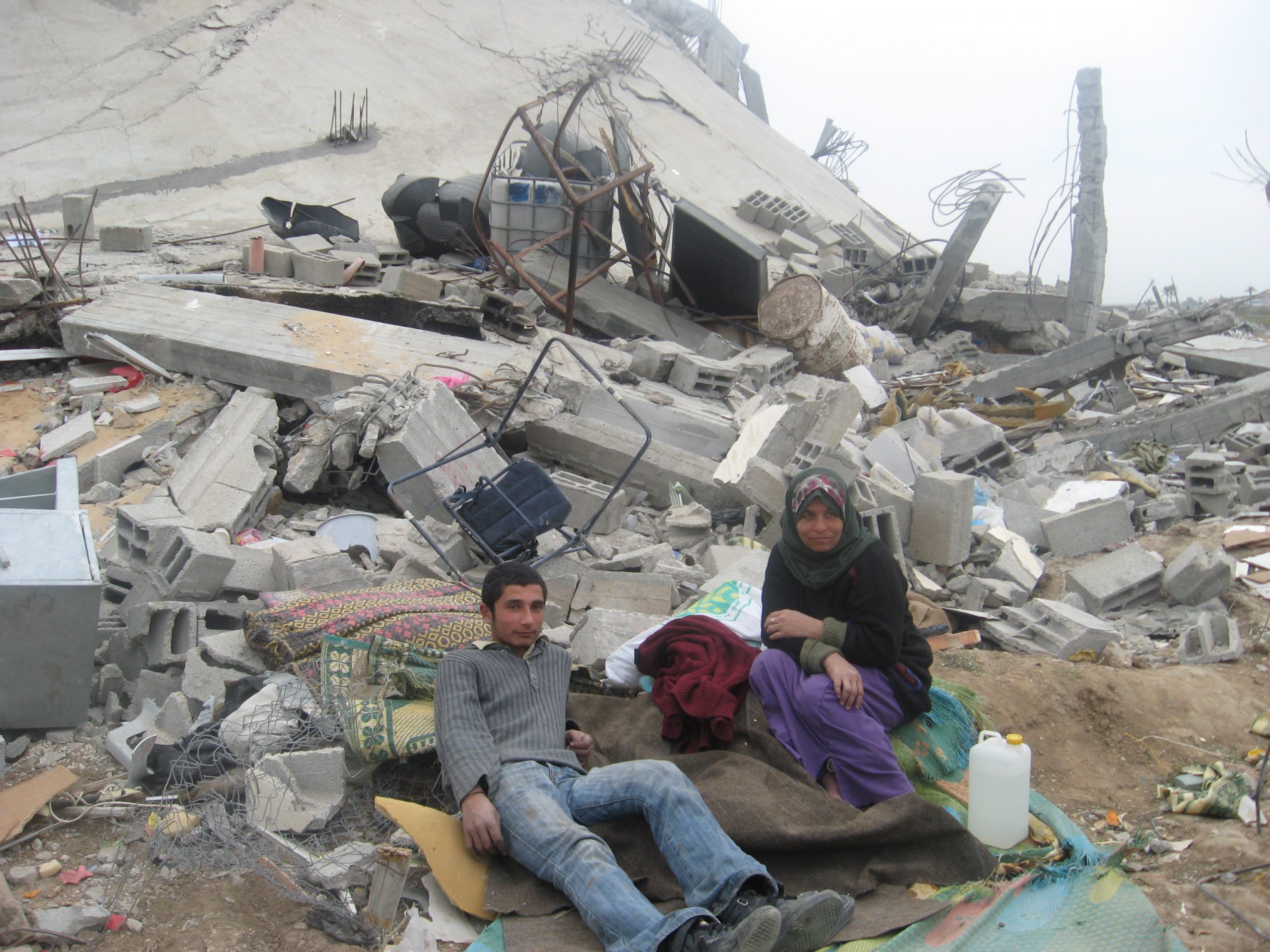 Tre innbyggere i Gaza sitter i ruiner avbygninger.