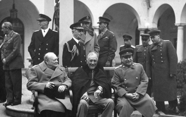 Churchill, Roosevelt og Stalin sitter på rad, i samtale.