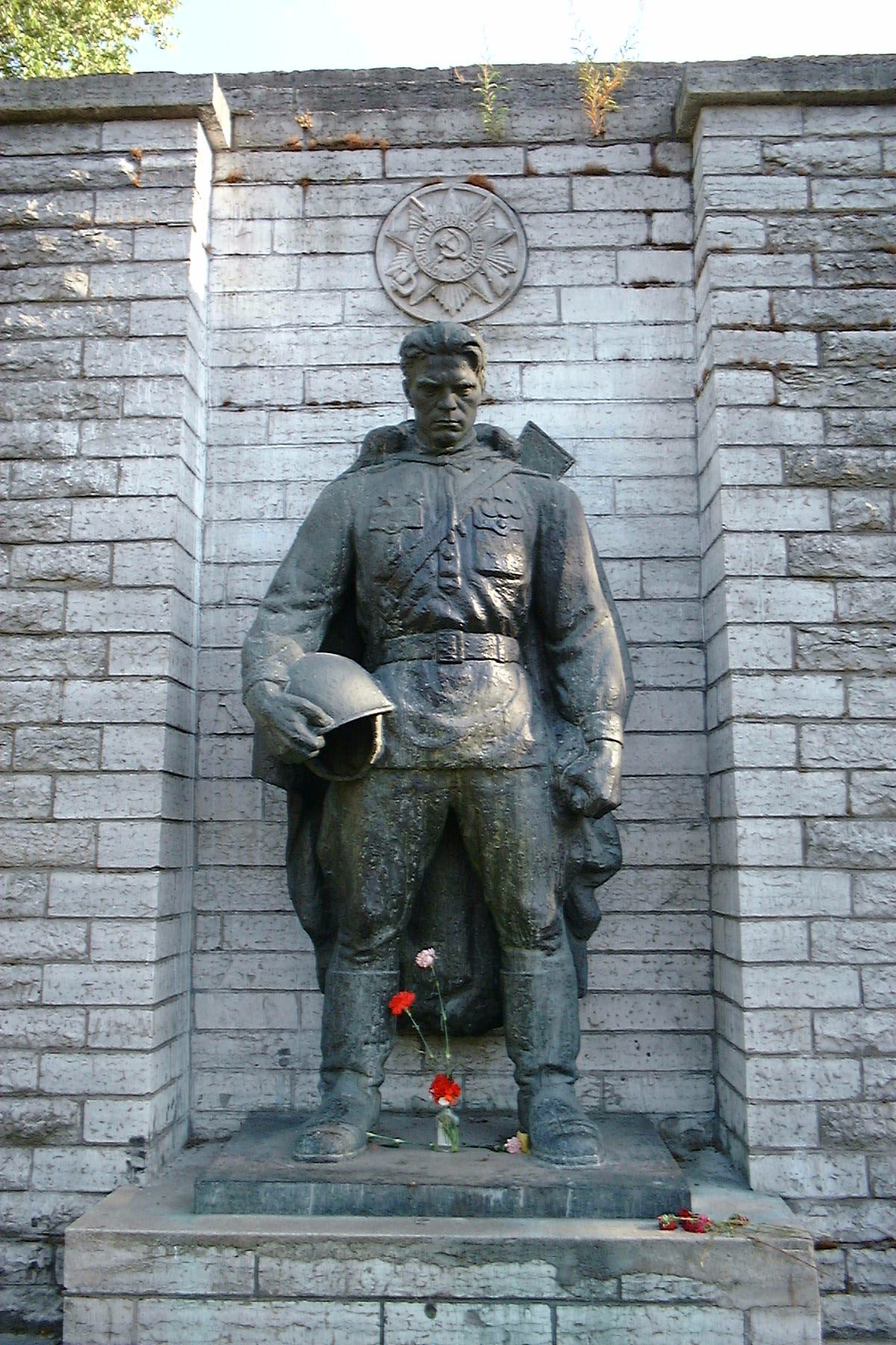 Statue av soldat med hjelm i hånden og noen blomster foran