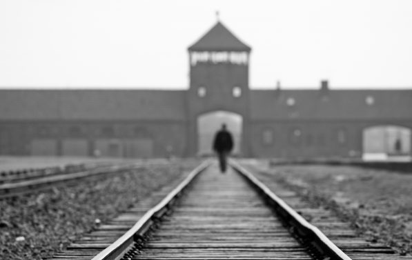 Svart-hvitt bilde tatt av en person som går langs togbanen som leder inn til Auschwitz