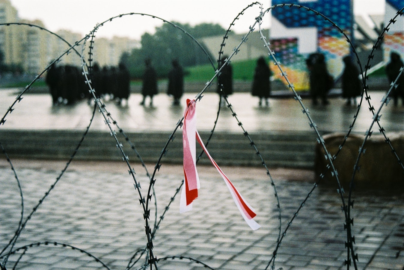 Piggtråd foran et torg. En sløyfe i de hviterussiske flaggfargene rødt og hvitt er knytt på gjerdet.