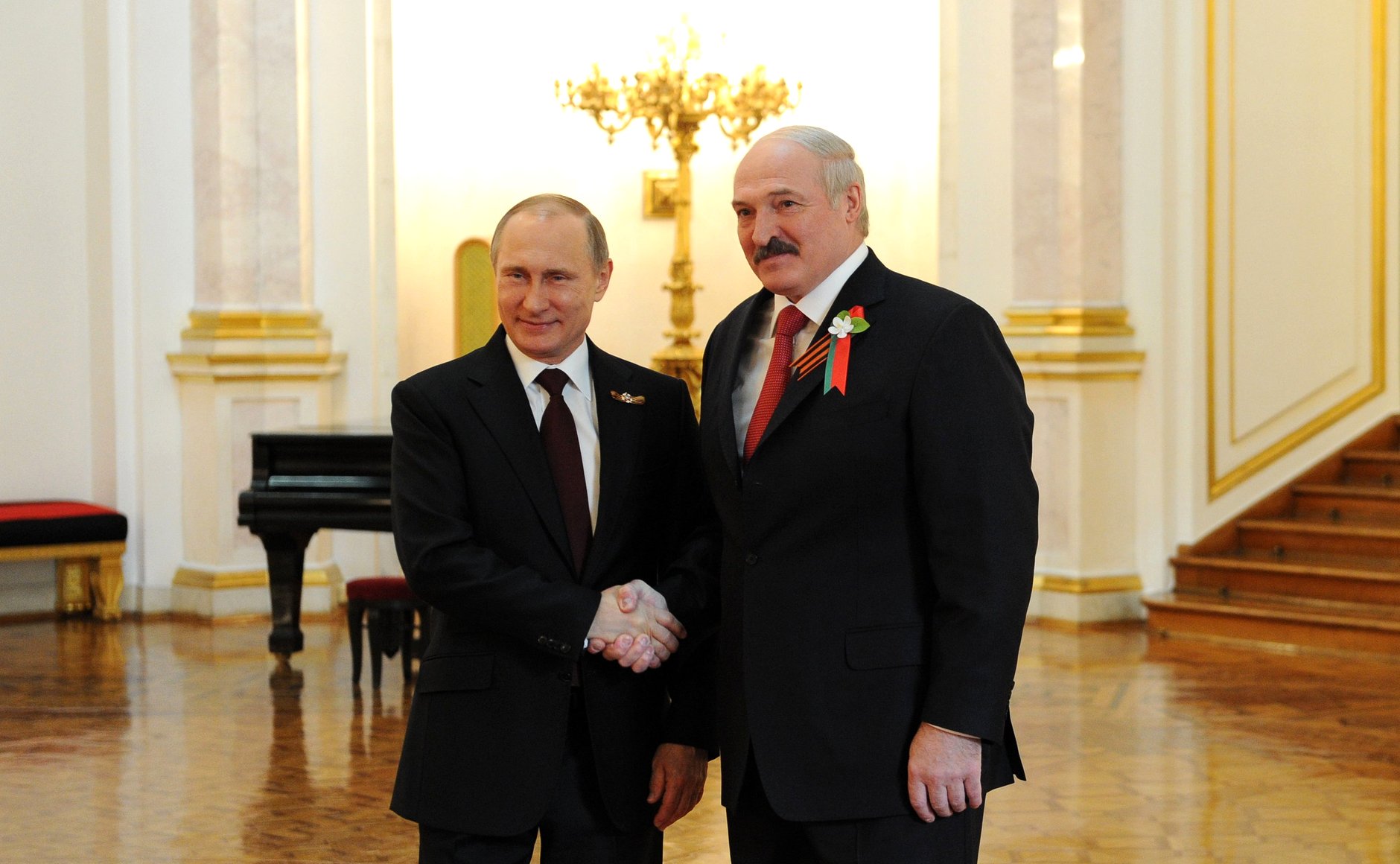 Putin og Lukasjenko står nære hverandre, og smiler under et håndtrykk.