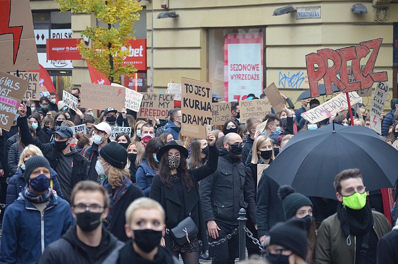 Mennesker med munnbind kledd i svart demonstrerer i en gate