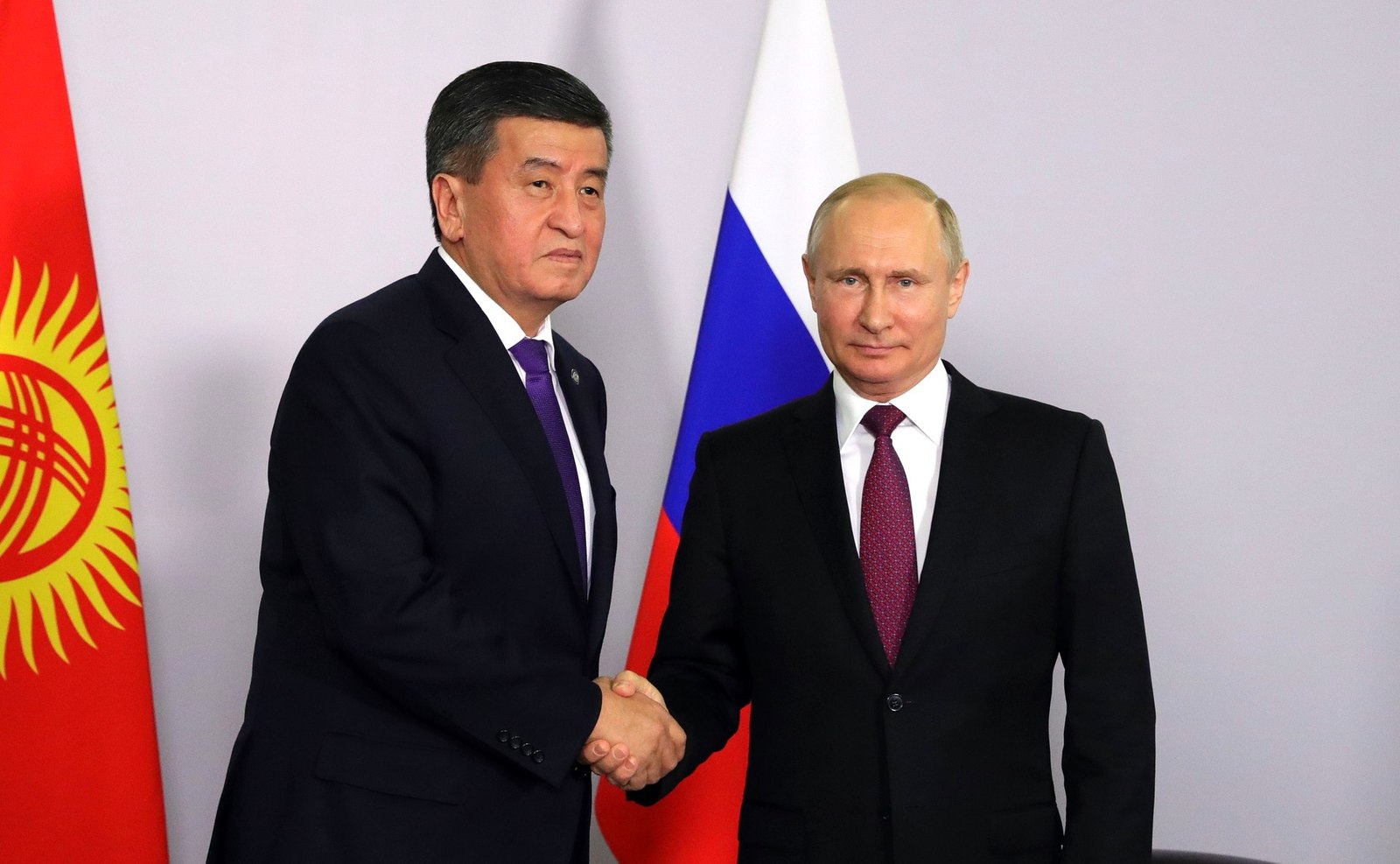 Jeenbekov og Putin tar hverandre i hendene foran et russiske og et kirgisisk flagg