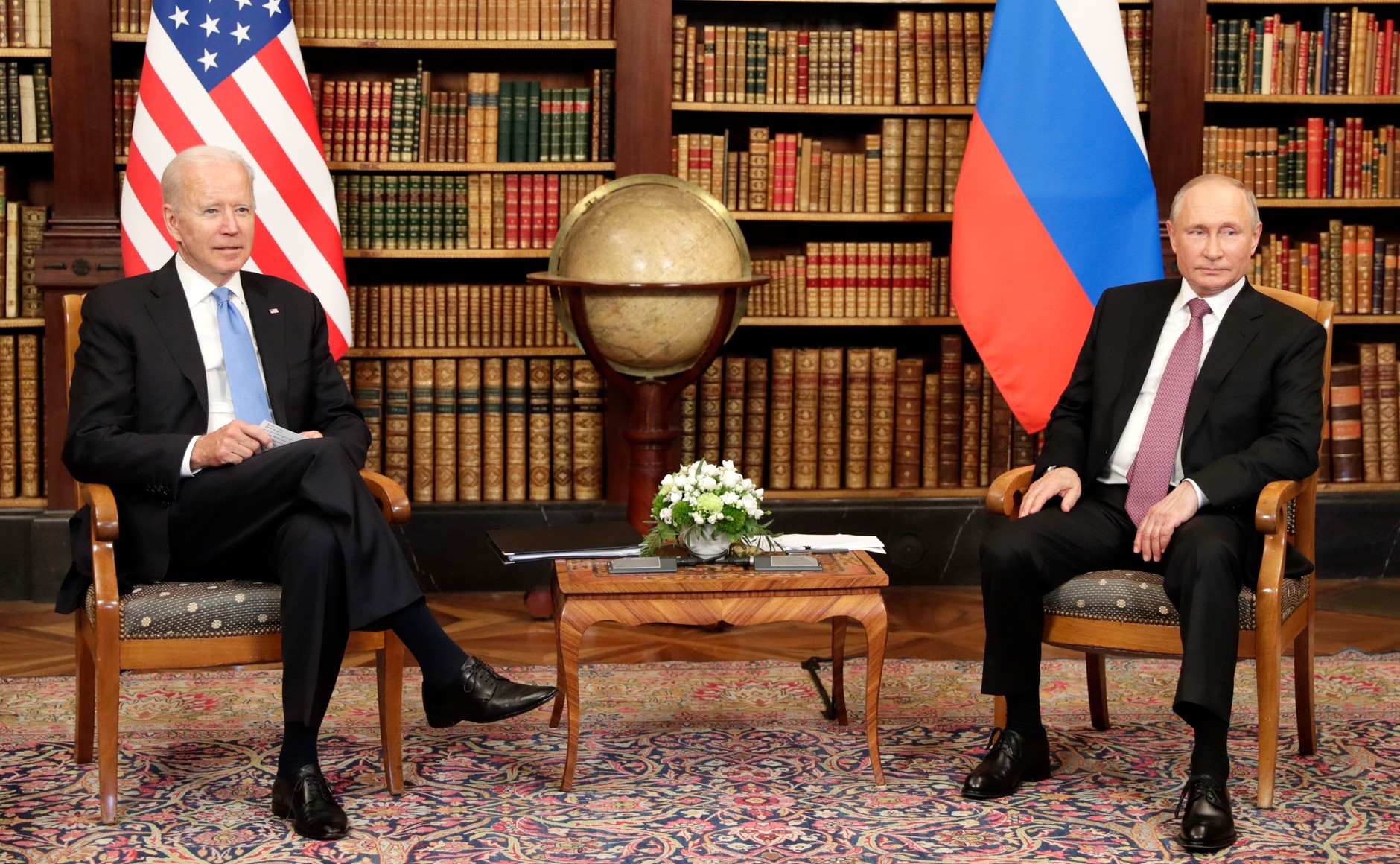 Biden og Putin sitter på hver sin side av en globus, med sine respektive flagg bak seg.