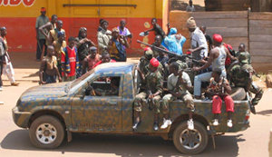 Bevæpnede menn kledd i militæruniform sitter på lasteplanet av en bil