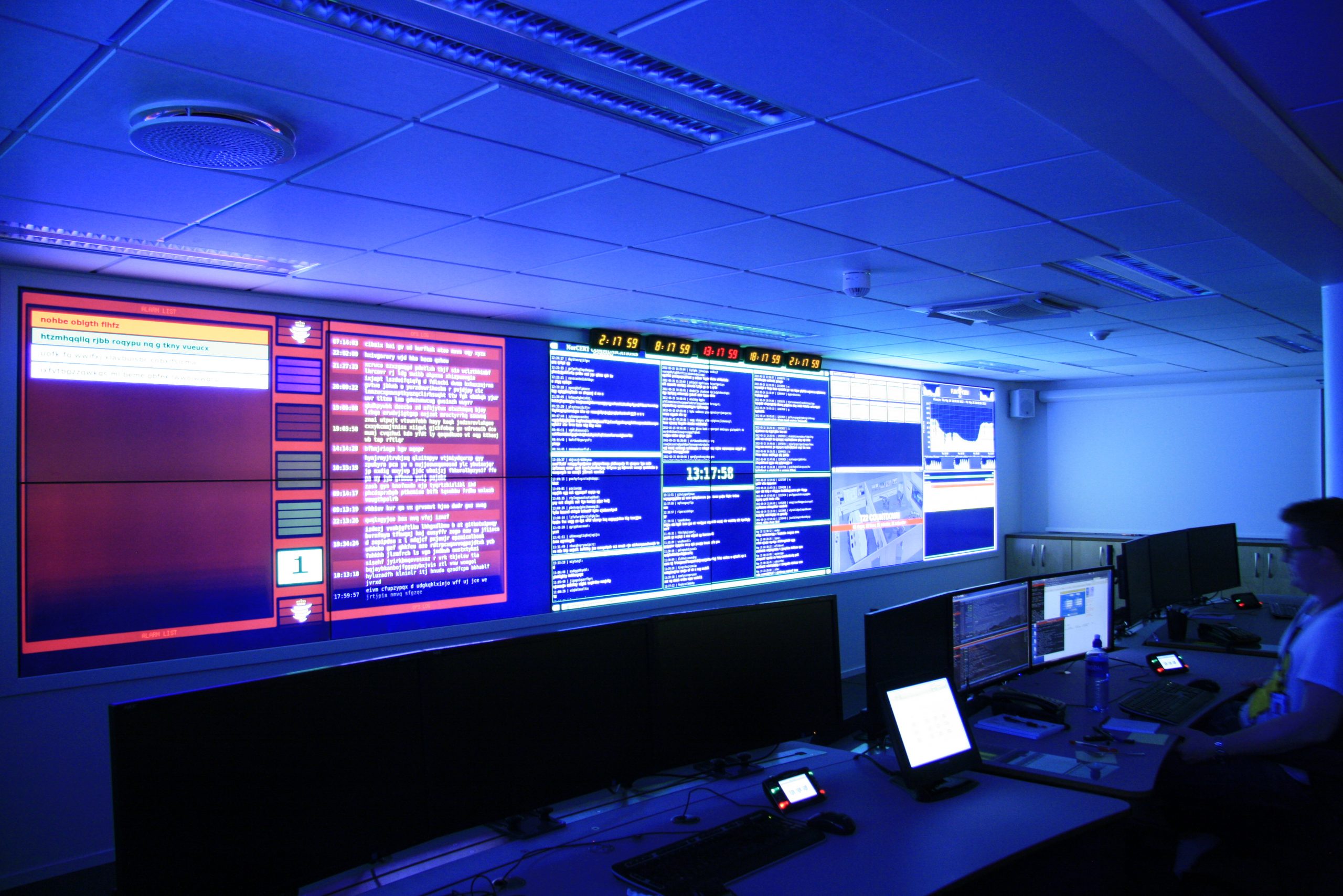 Bildet viser flere skjermer i et mørkt rom, som lyses opp i blått fra de prosjekterte dataskjermene. I midten sees en nedtellingsklokke.