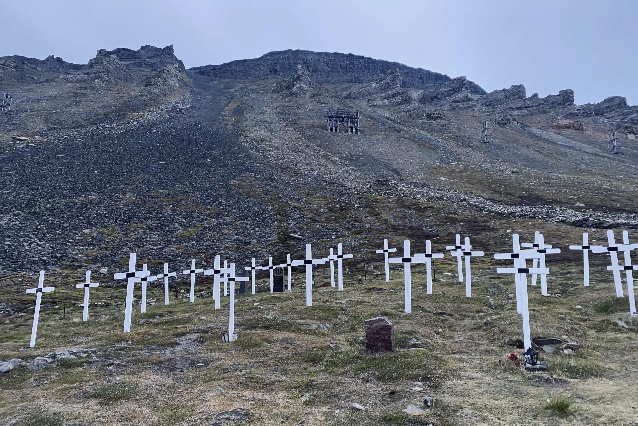 En rekke hvite kors plassert i bunnen av fjellsiden. Gruveheiser i bakgrunnen.