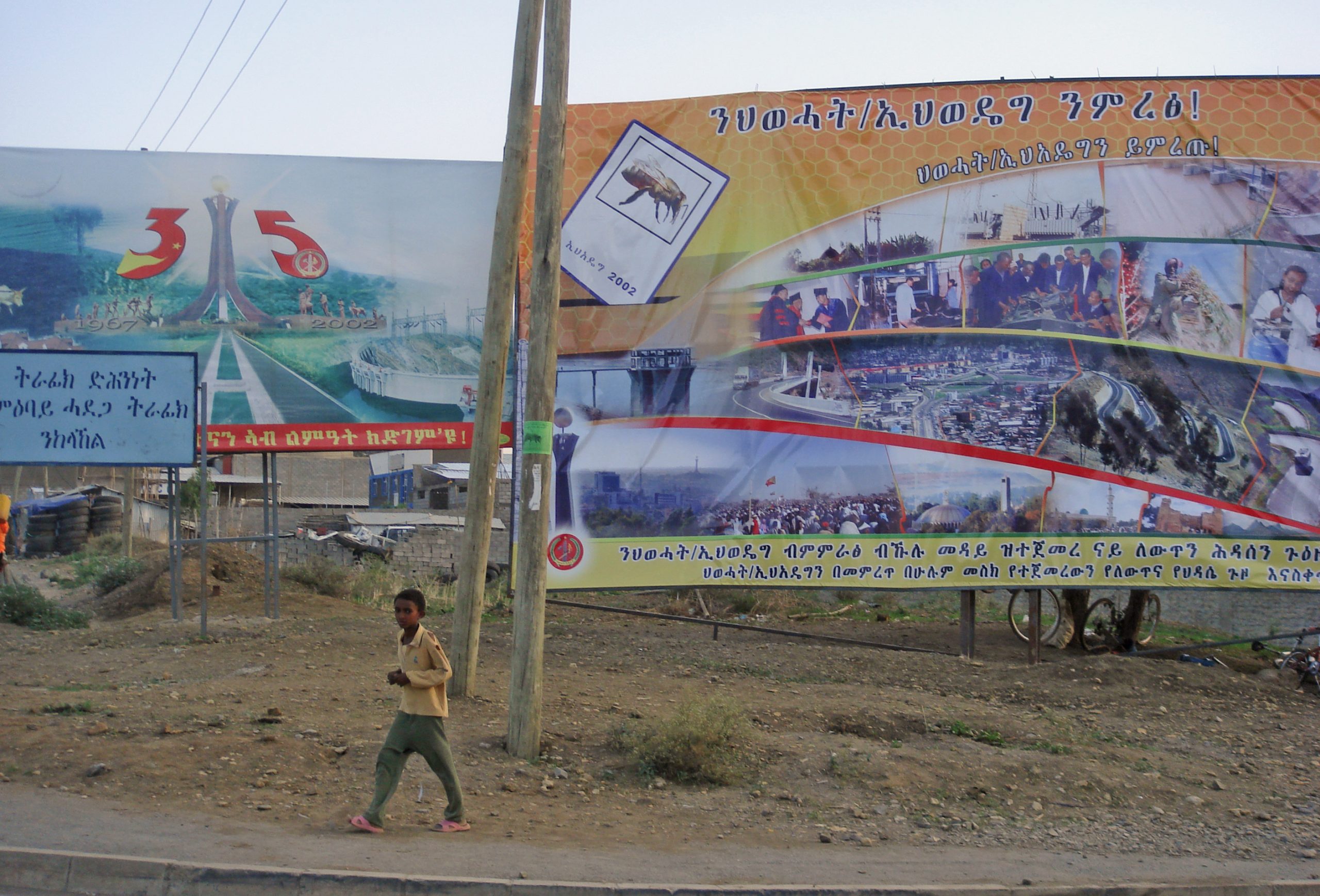 To store reklameplakater for henholdsvis TPLF og EPRDF, og en liten gutt som rusler foran dem. 