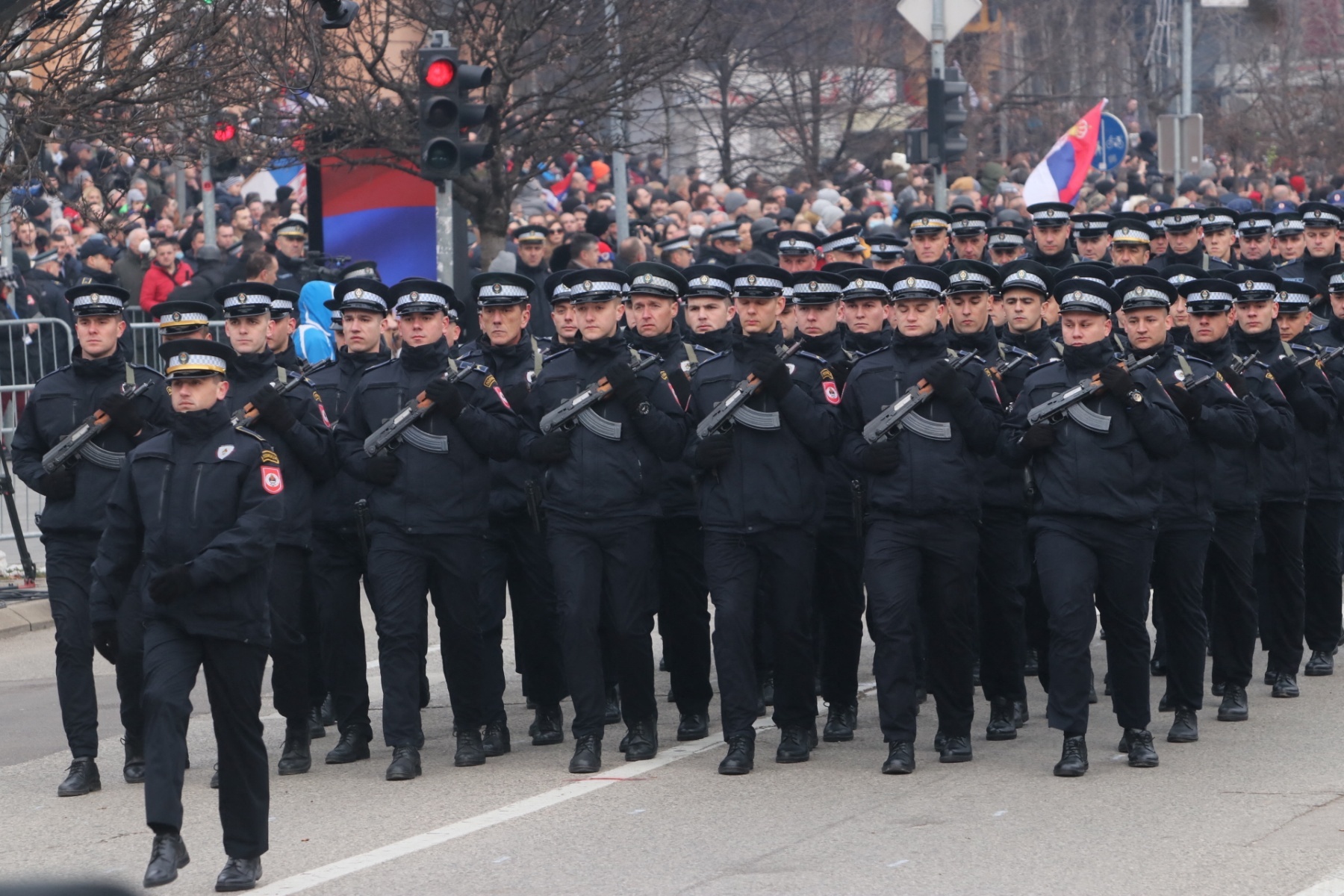 Uniformerte og bevæpnede politifolk marsjerer taktfast. Et stort publikum ser på. Flere av Republika Srpskas flagg skimtes omkring.