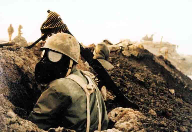 bildet viser en soldat med gassmaske  som sitter bak en skyttegrav