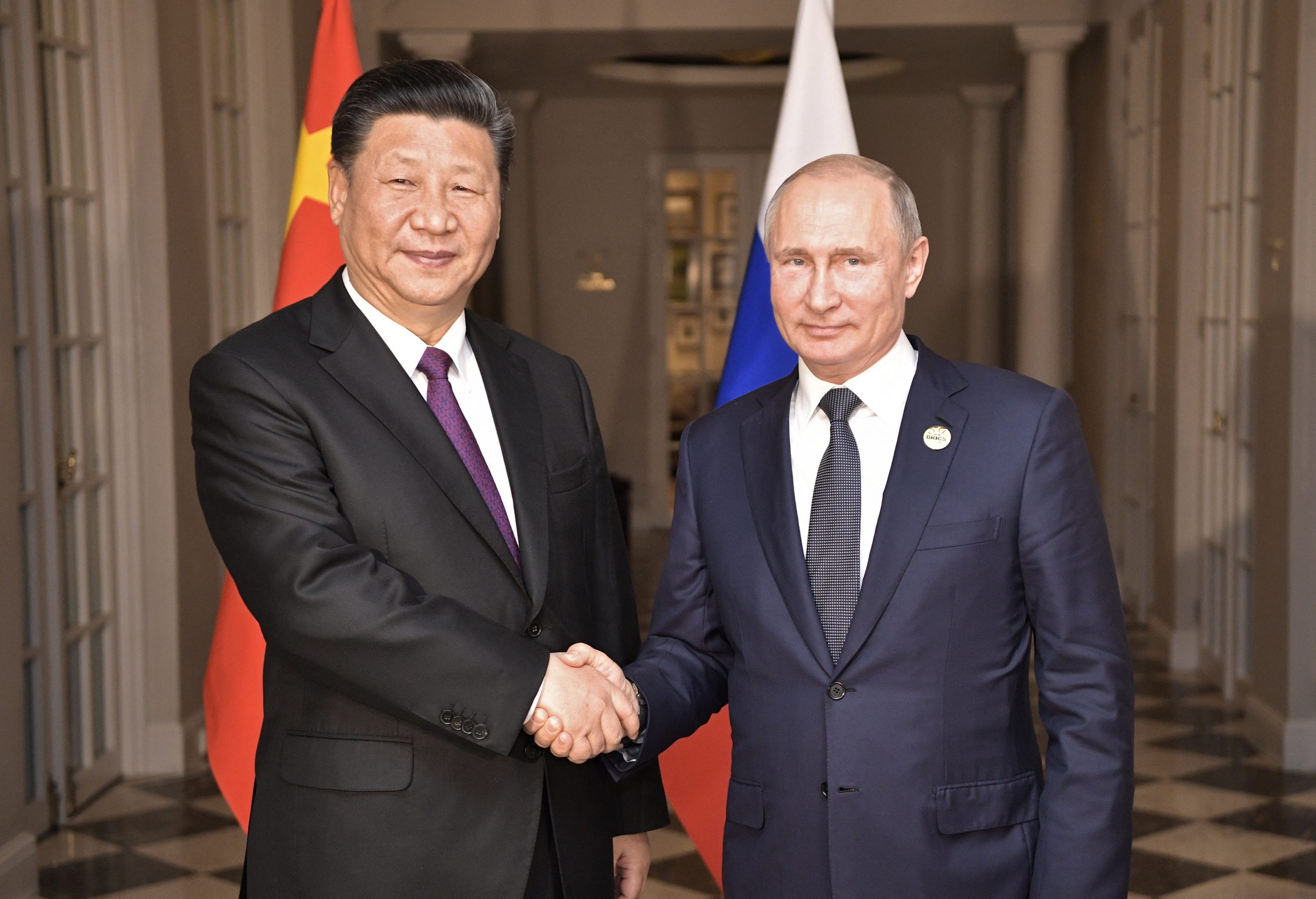 Russlands president Vladimir Putin og Kinas president Xi Jinping håndhilser for Kina og Russlands flagg.